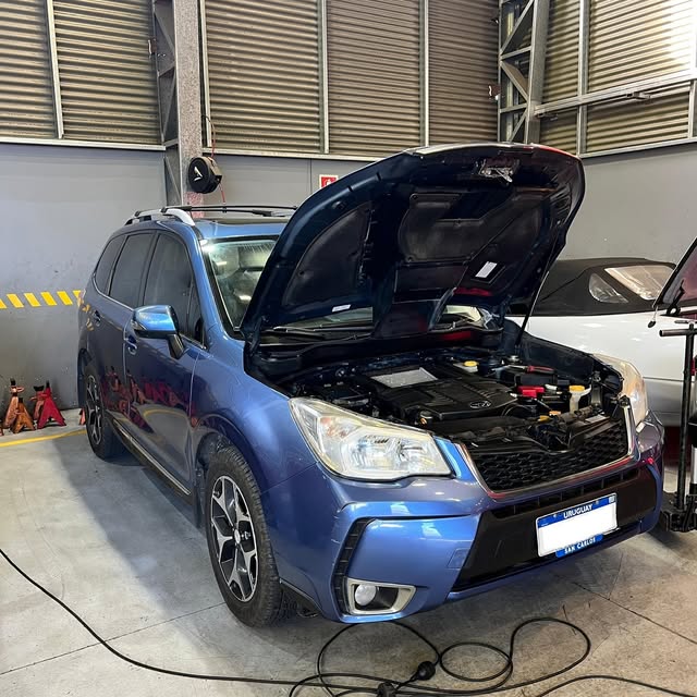 Subaru Forester azul con el capó abierto y el motor visible en el taller